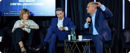 Trois personnes en discussion lors d’un panel sur l’industrie spatiale avec un écran en arrière-plan.