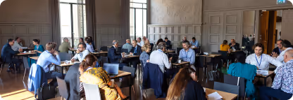 Personnes discutant et travaillant sur des ordinateurs portables dans une grande salle précise.