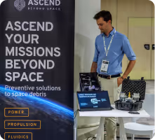 Un homme en chemise bleue examine un équipement sur une table à côté d'une affiche Ascend Techno Space.