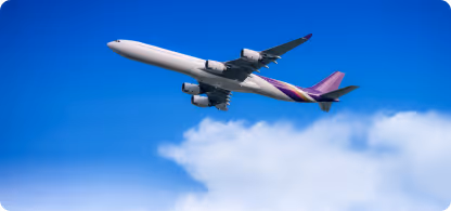 Un avion blanc avec une queue violette vole dans un ciel bleu avec quelques nuages blancs.