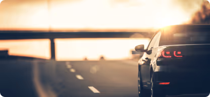 Voiture noire sur une route au coucher du soleil avec un pont en arrière-plan.