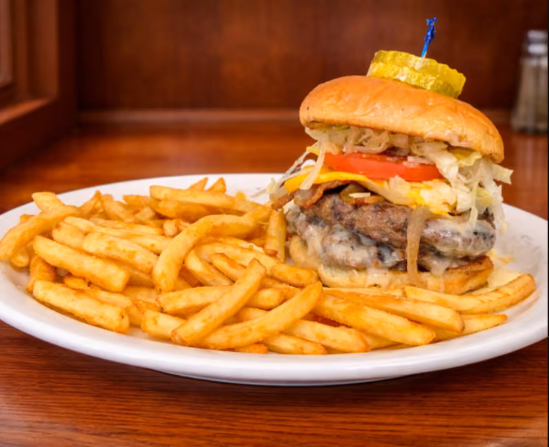 Cheeseburger with lettuce, tomato, and pickles served with golden fries on a white plate.