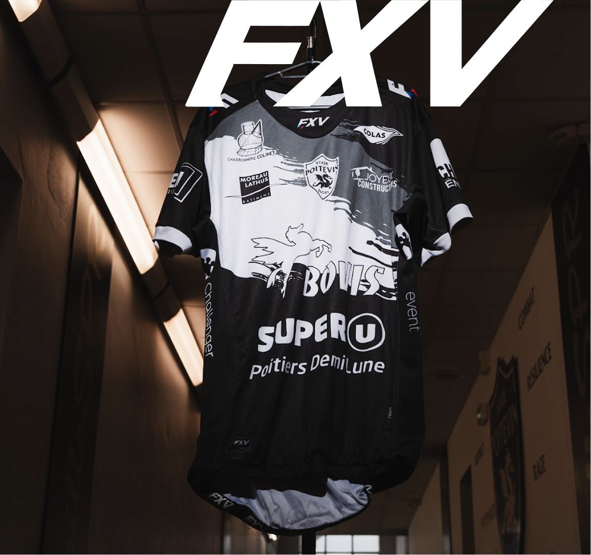 Black and white sports jersey with multiple sponsor logos, including SUPER U and Stade Poitevin, hanging on a hanger in a dimly lit corridor.