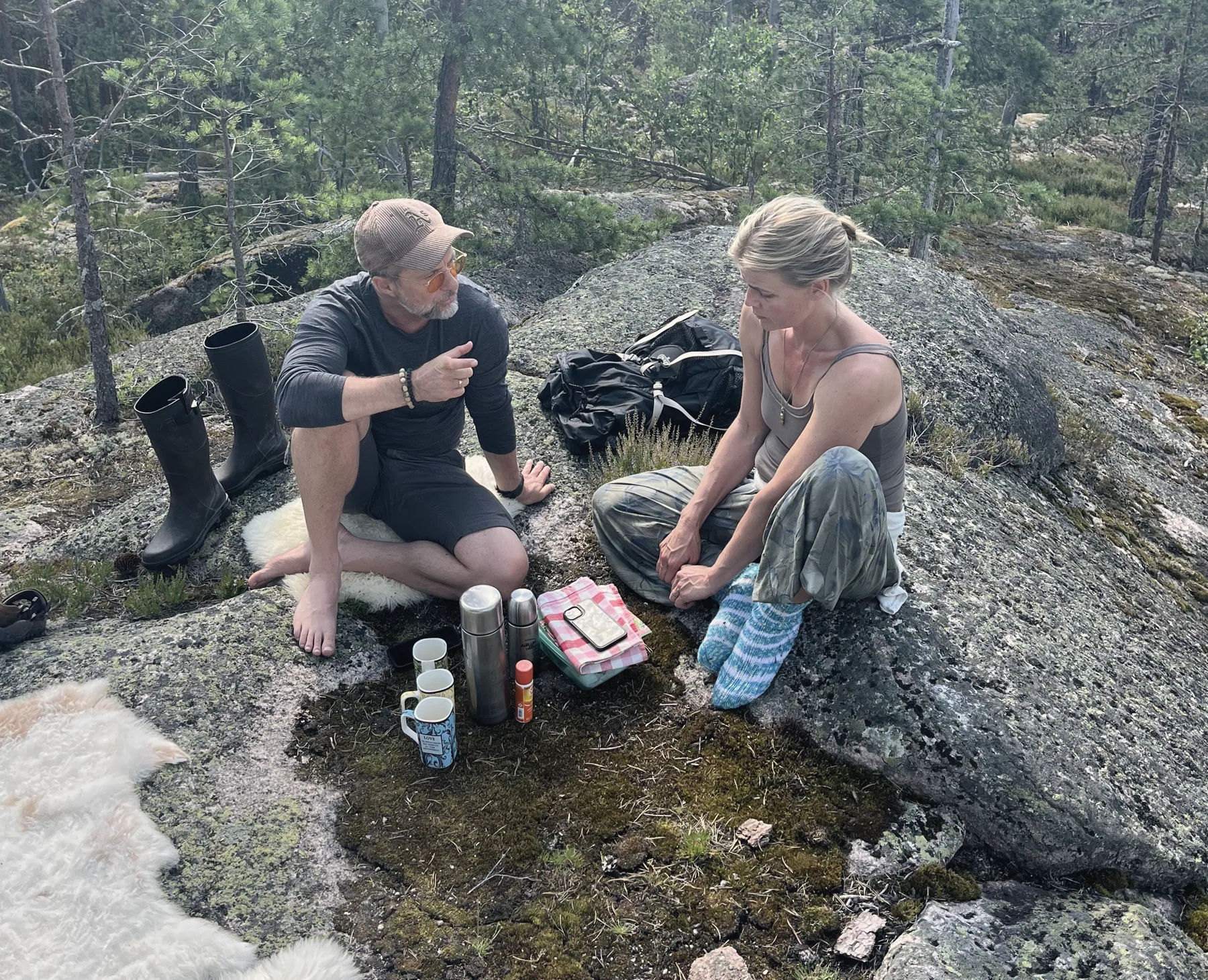 Zwei Menschen sitzen auf einem Felsen in der finnischen Natur und sprechen miteinander
