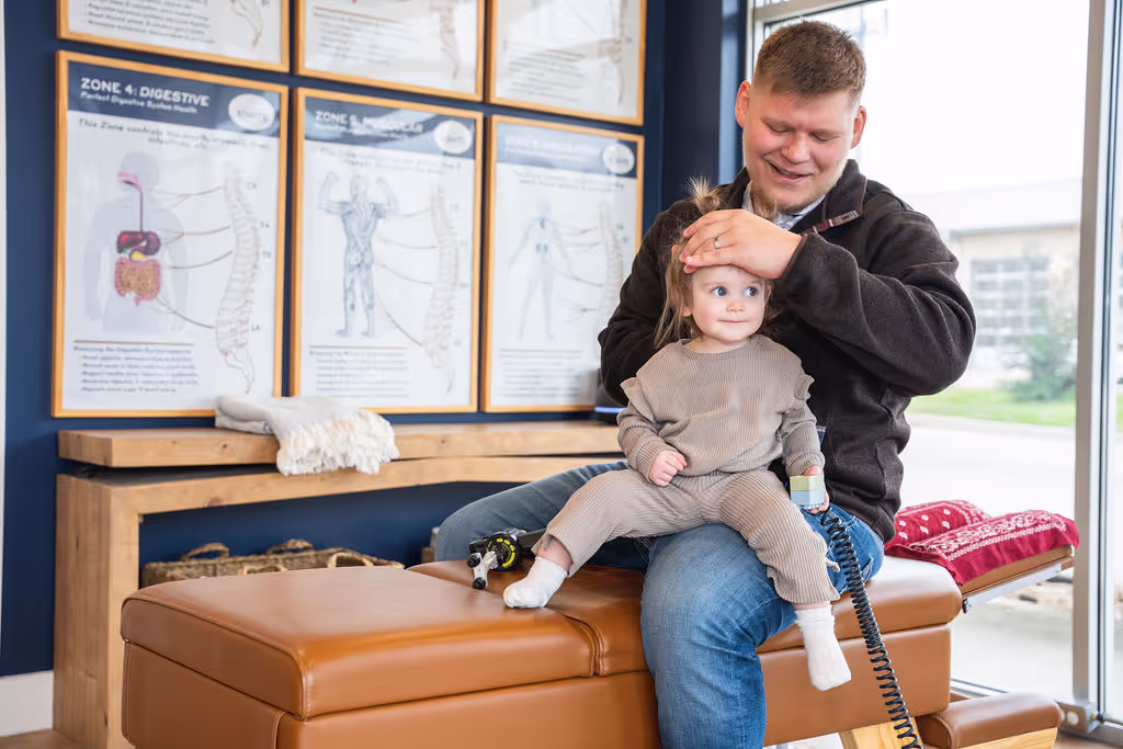 Happy baby smiling with family chiropractor during infant wellness visit