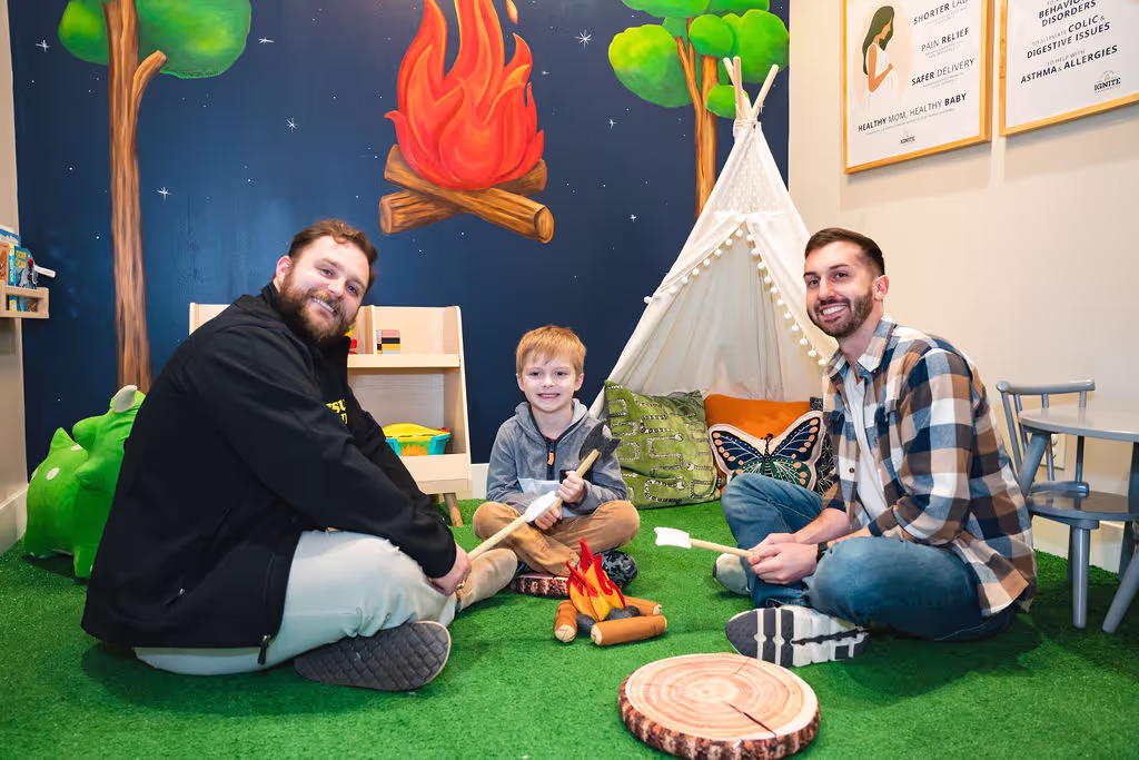 Family gathering around campfire in pediatric chiropractic play area Cypress