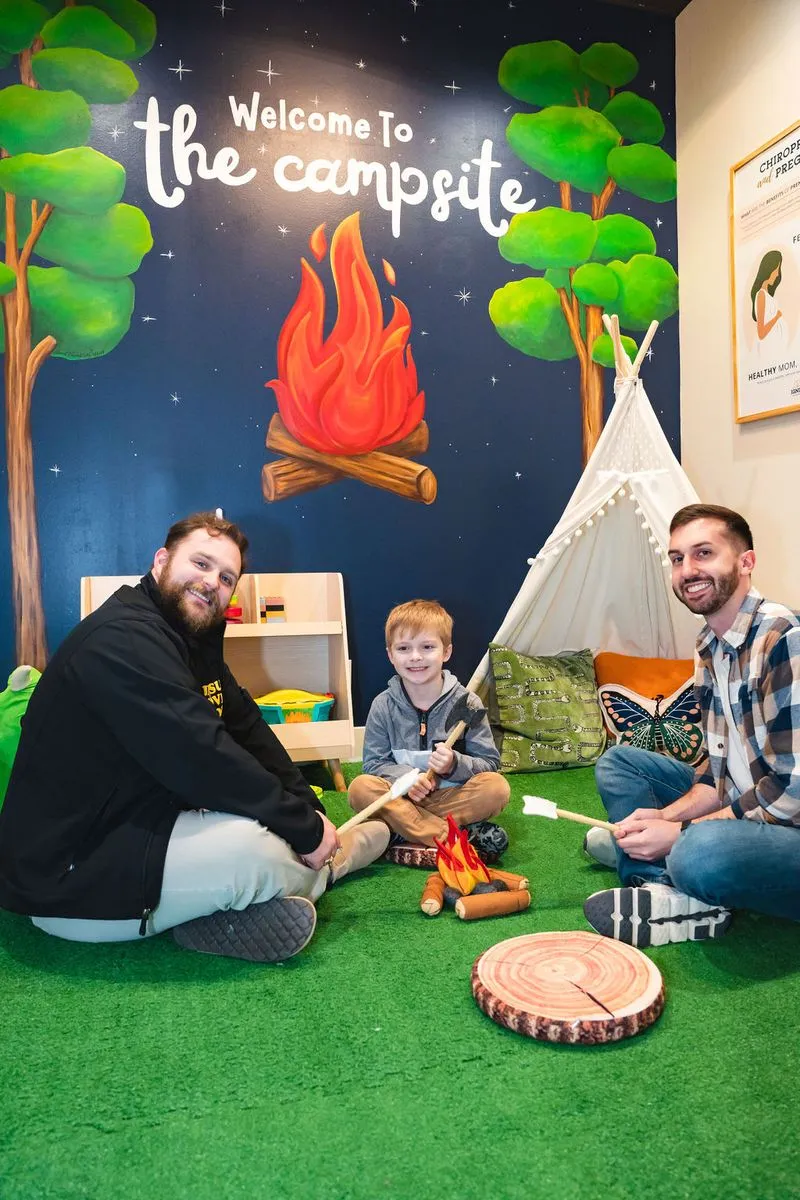 Families smiling around campfire in pediatric chiropractic kid-friendly play area