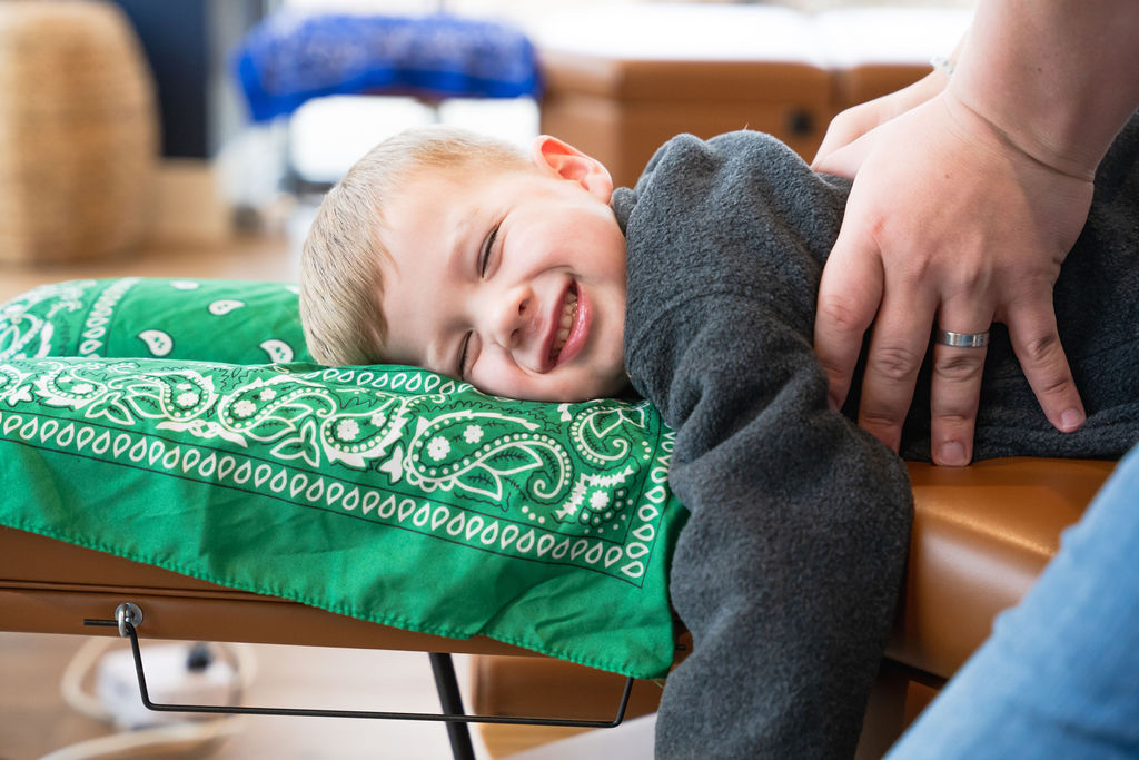 A child smiling as he gets adjusted by a chiropractor near Haslet, TX.