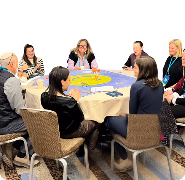Group of people smiling and engaged around a round table with a colorful board game or activity.