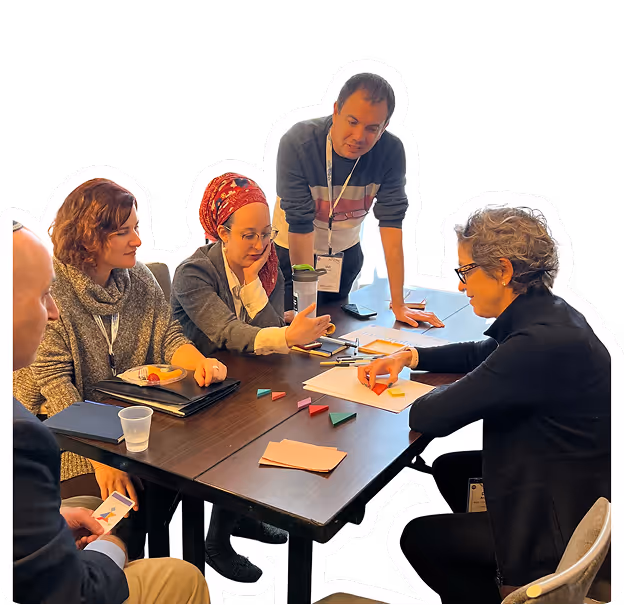 Five diverse adults engaged in a collaborative meeting around a conference table with papers and colored sticky notes.