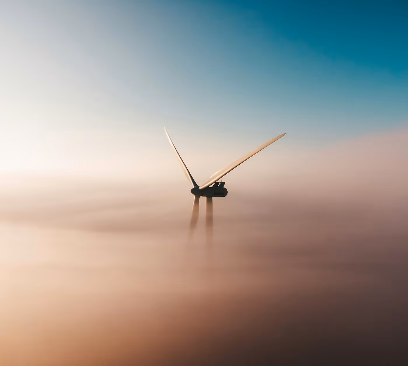 Wind turbine blades partially visible above dense fog under a clear sky.