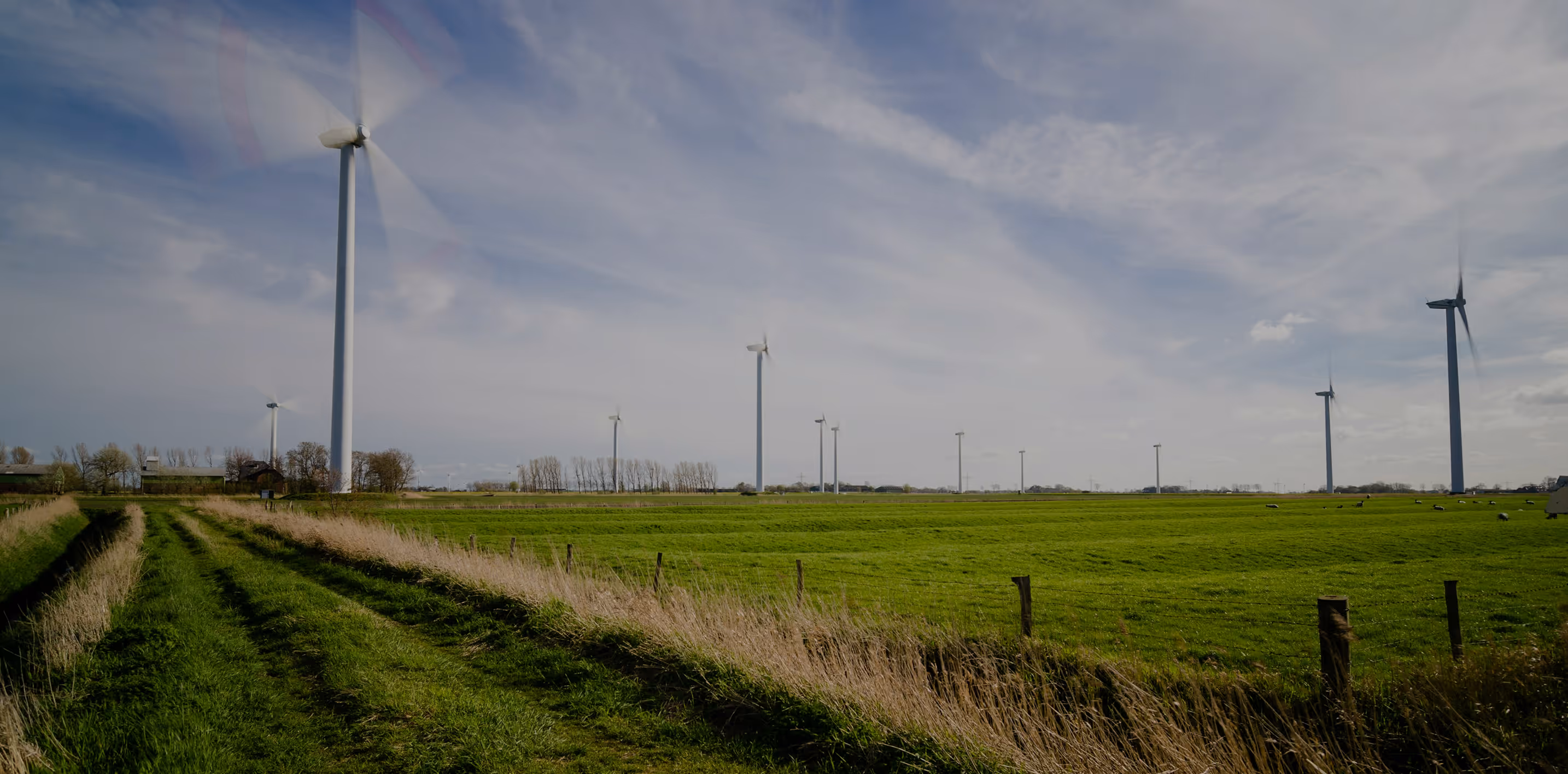 Green rural landscape with multiple wind turbines spinning under a partly cloudy sky.