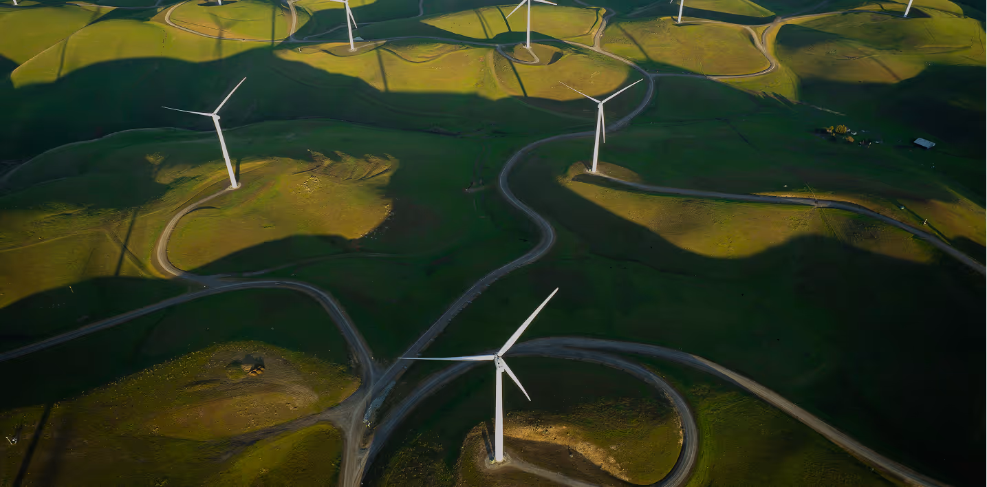 Aerial view of wind turbines scattered across green rolling hills with winding dirt roads.