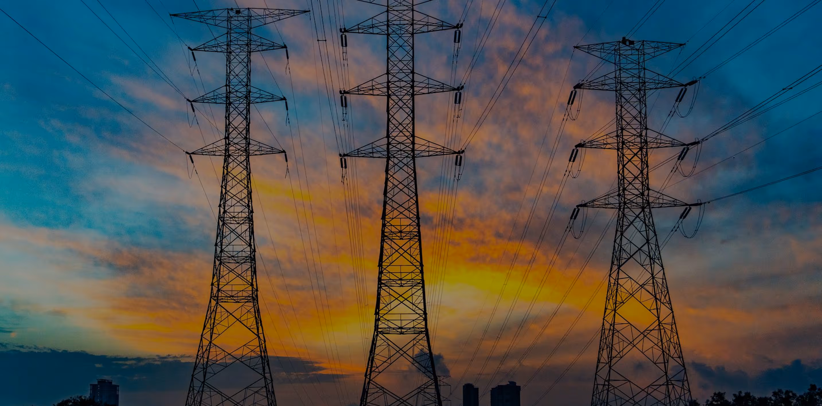 Three high-voltage electricity transmission towers silhouetted against a colorful sunset sky.