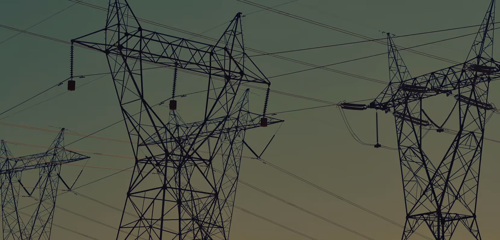 Multiple high-voltage electricity transmission towers with power lines against a dusky sky.