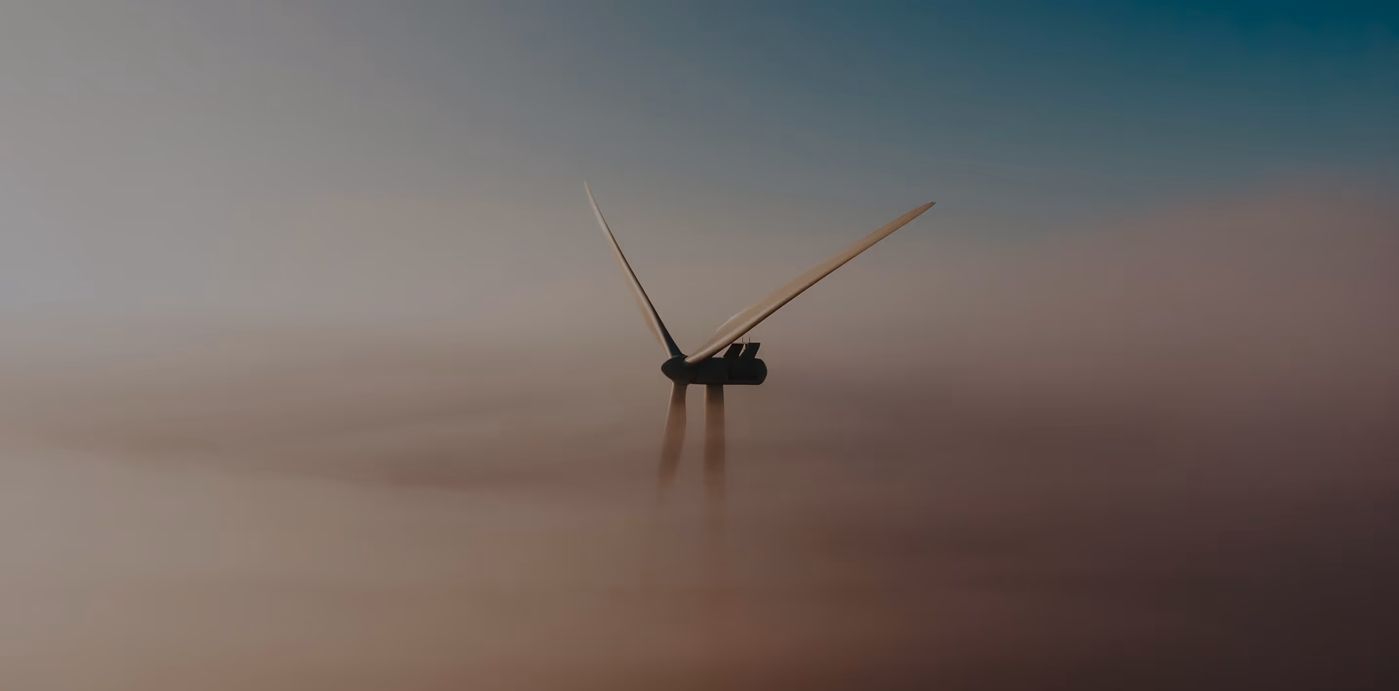 Wind turbine blades turning above a thick layer of fog under a clear sky.