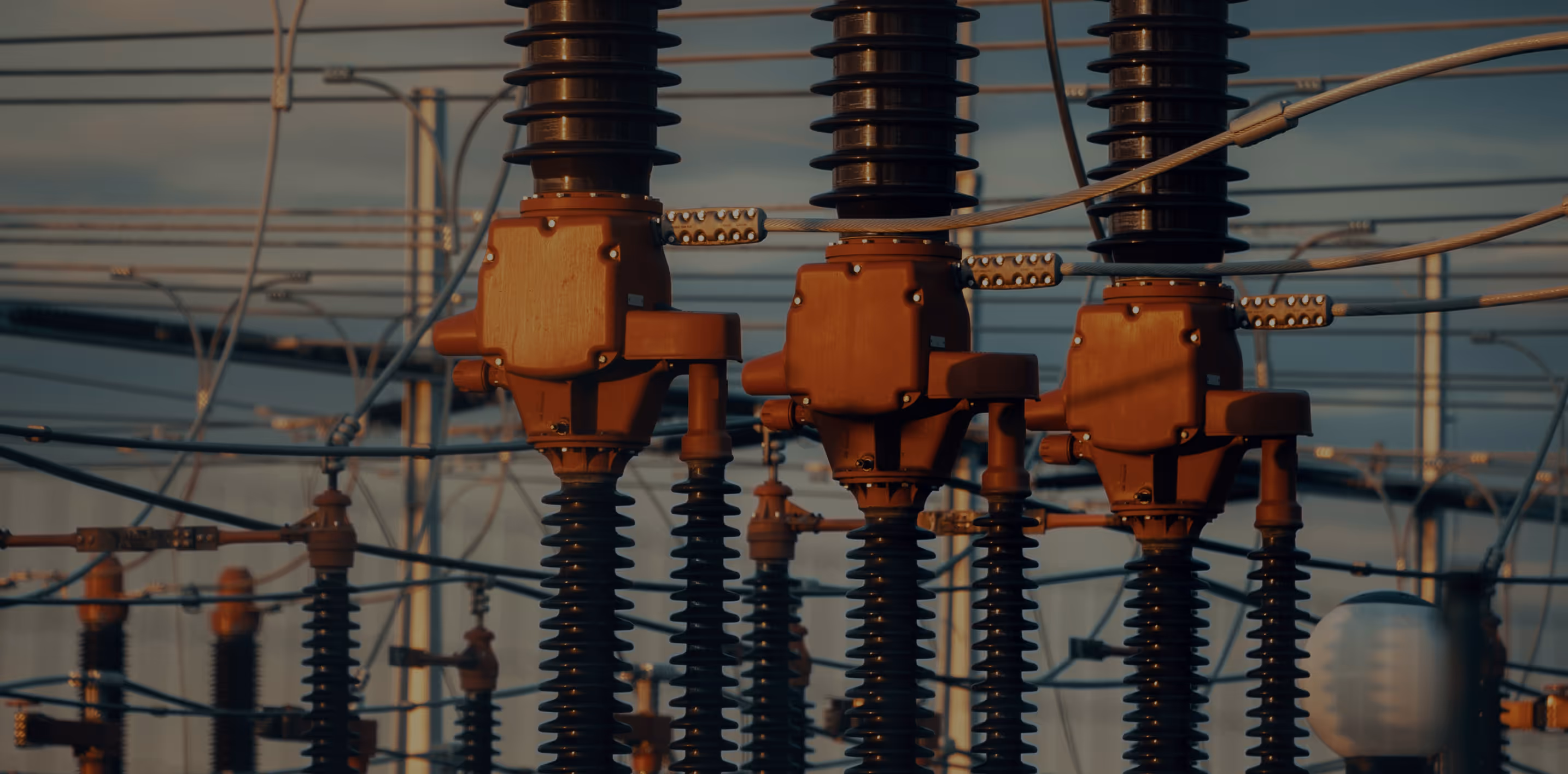 Close-up of electrical insulators and connectors on high voltage power lines at sunset.