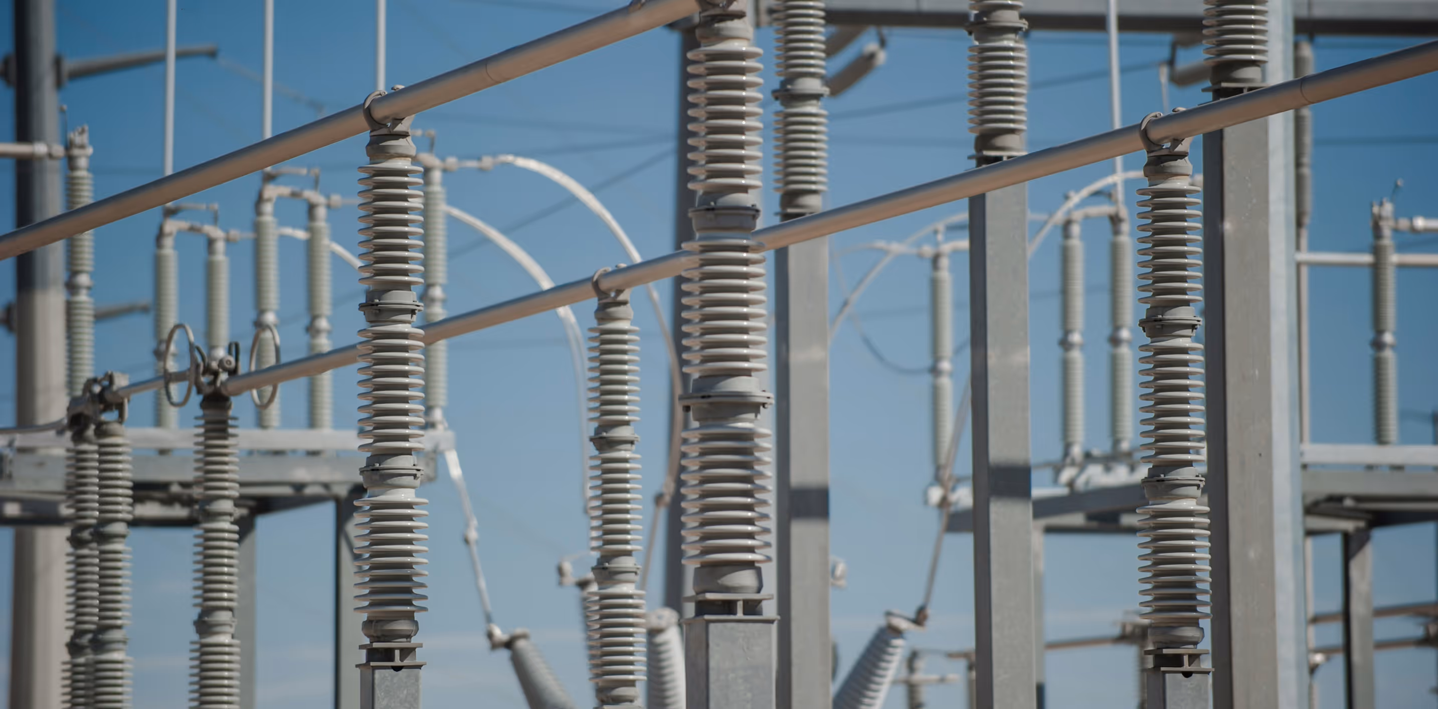 Close-up of insulators and metal structures at an outdoor electrical substation under a clear blue sky.