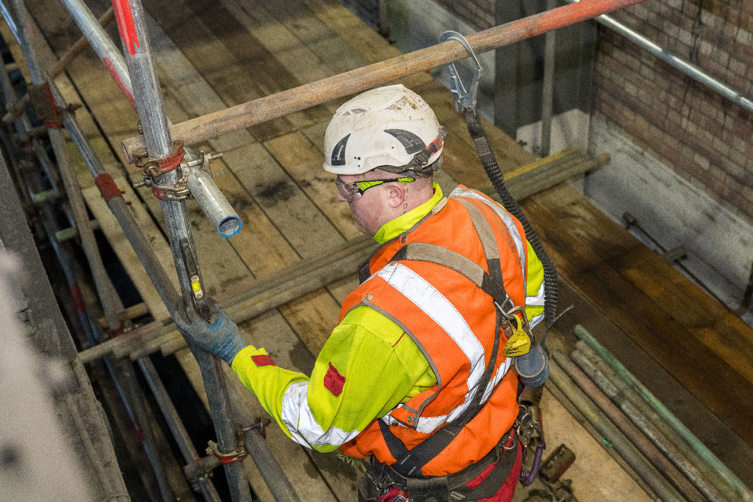 Construction worker in safety gear assembling scaffolding at a building site.