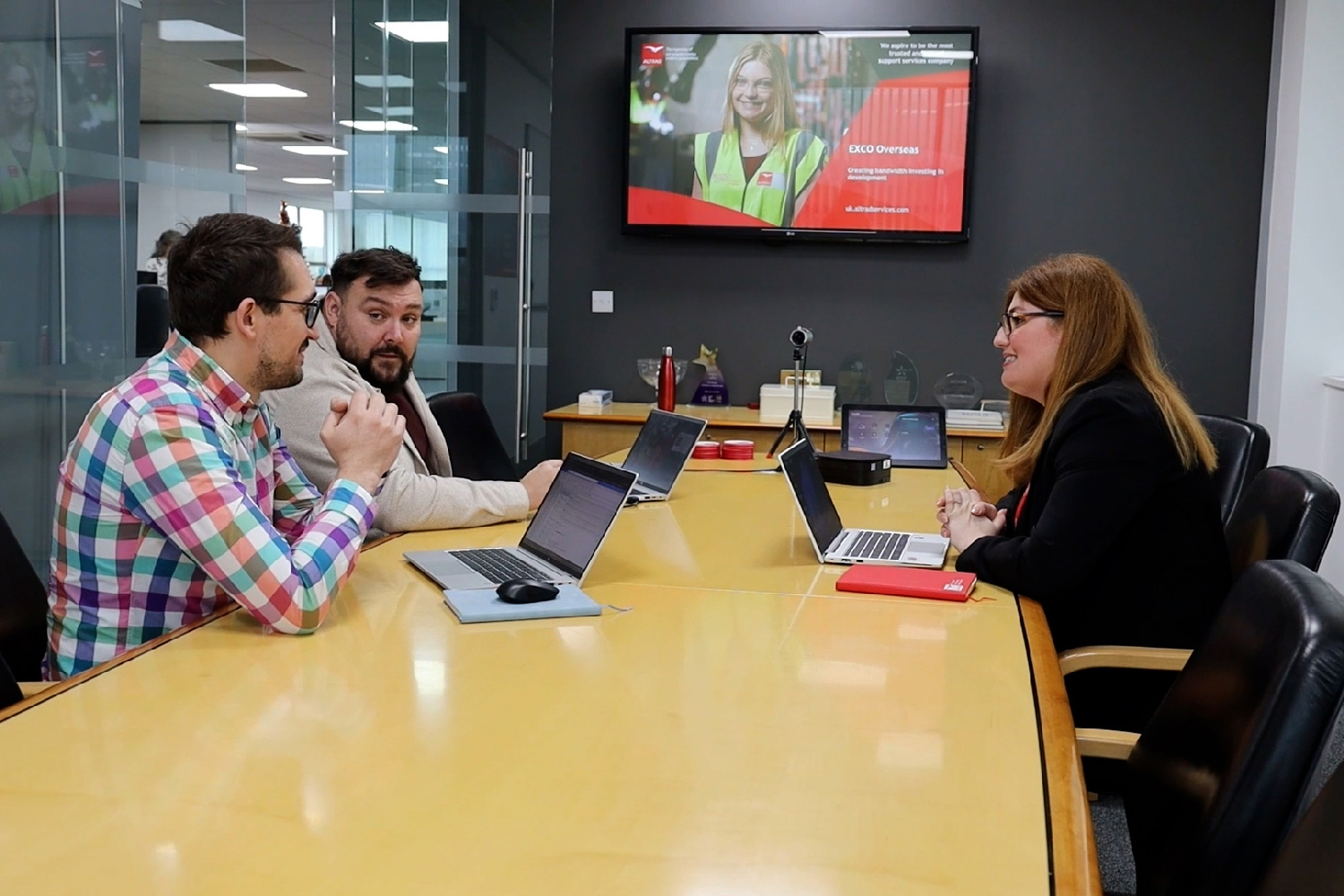 Three colleagues having meeting at a conference table with laptops in a modern office room.