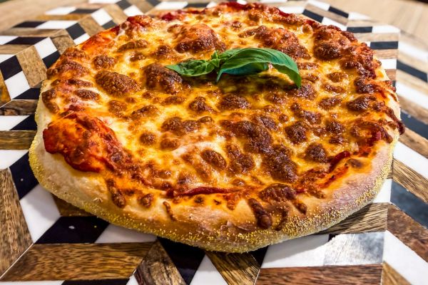 Close-up of a cheese pizza with a basil leaf on top on a patterned wooden and black-and-white plate.