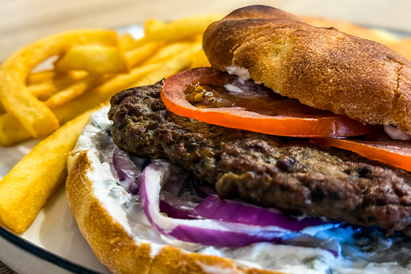 Close-up of a burger with grilled beef patty, tomato slices, red onion, and mayonnaise on a toasted bun, served with thick-cut fries.