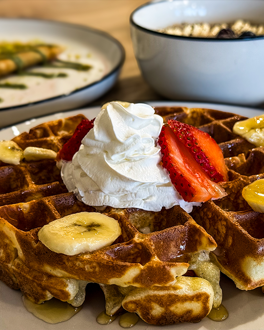 Freshly pressed Belgian waffle with whipped cream and sliced strawberries