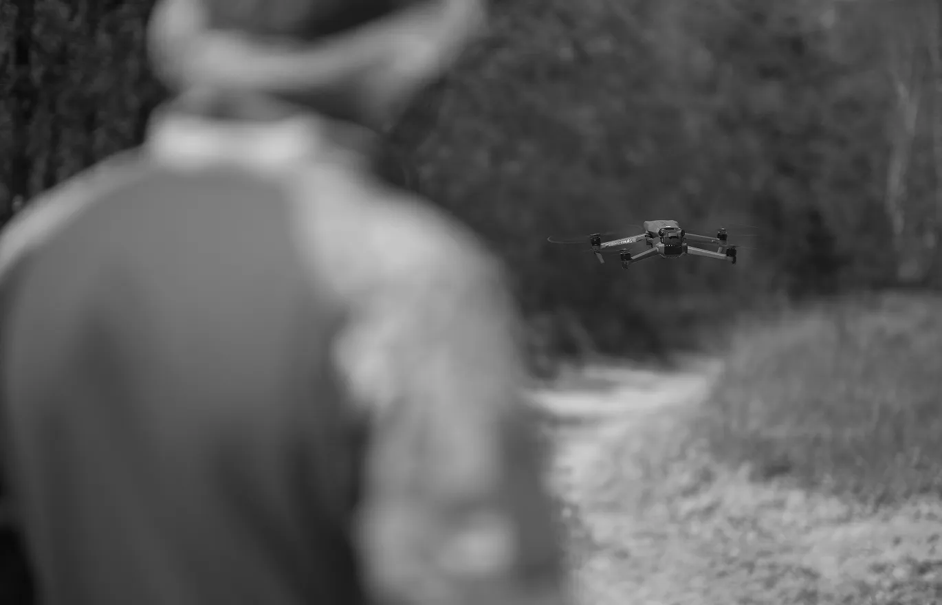 Osoba sterująca dronem latającym nad ścieżką w lesie.