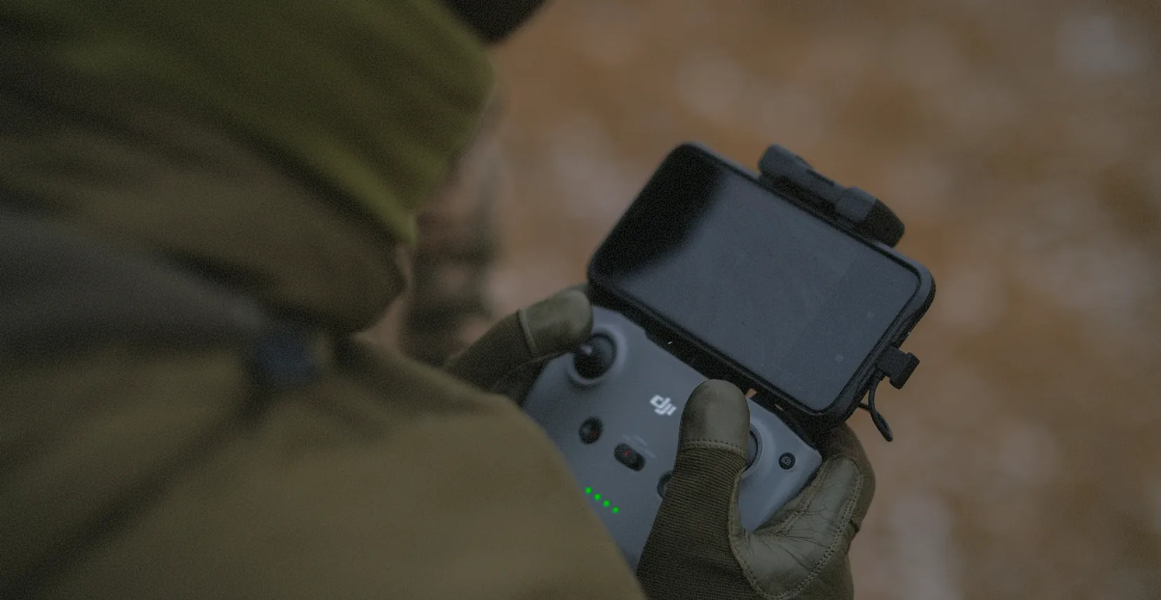 Osoba w rękawicach trzymająca pilot drona z ekranem smartfona.