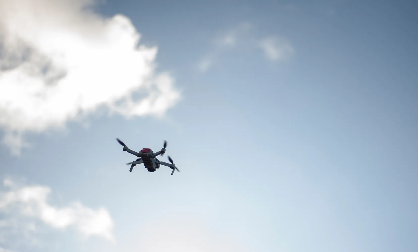 Dron latający na niebie z kilkoma białymi chmurami w tle.