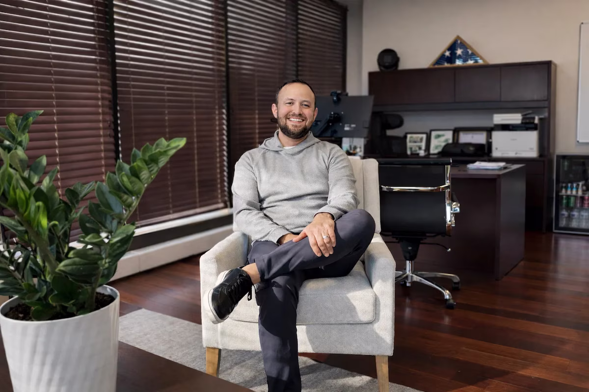 Robert Lopez, CFP smiling in gray hoodie sitting cross-legged on armchair in modern office with wooden floors.