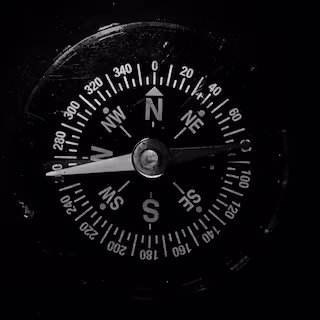 Black and white close-up of a compass showing directions and degrees with needle pointing east.