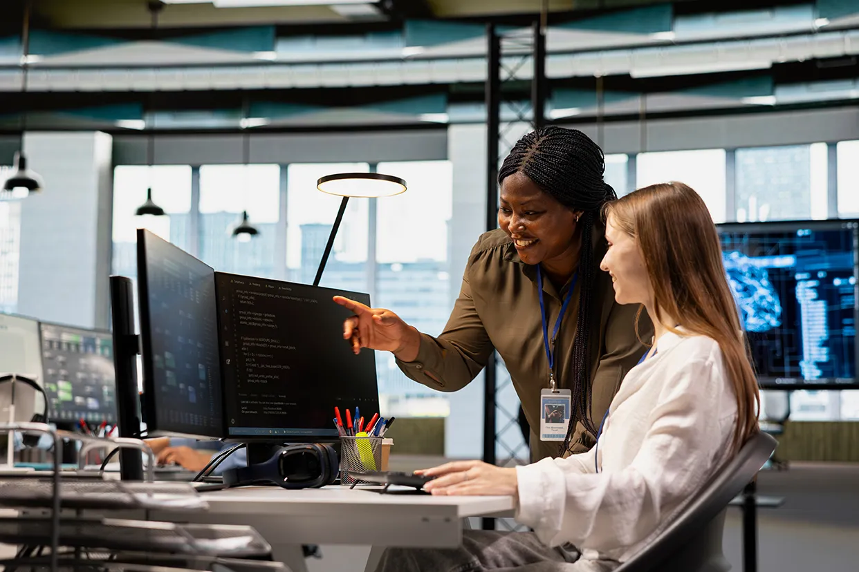 Five diverse students smiling and working together on a laptop in a well-lit library with bookshelves in the background, two giving a high five.