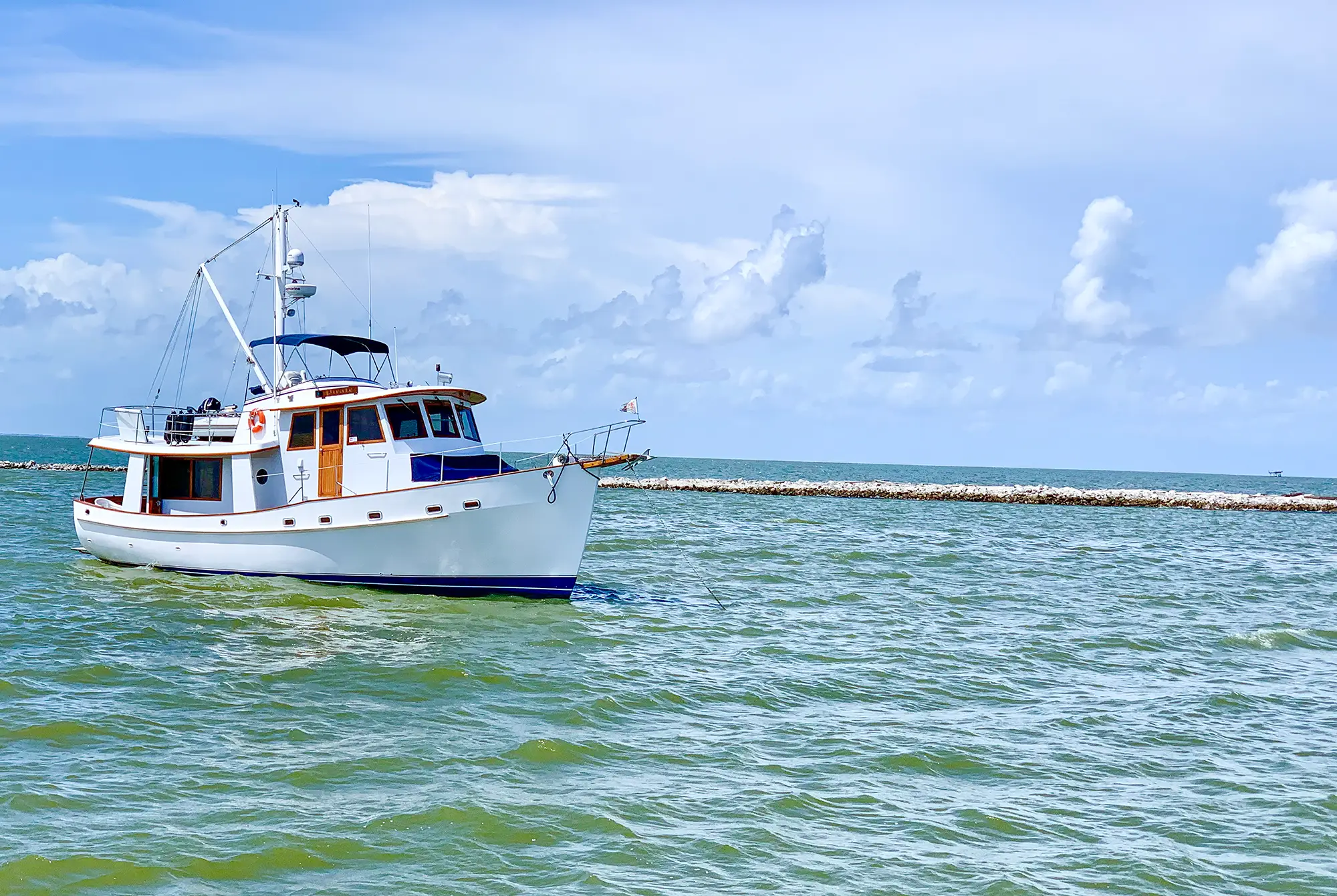 White motor yacht anchored in calm blue-green ocean waters under a partly cloudy sky.