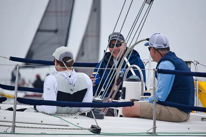 Three men sitting and chatting on a sailboat during a sailing event.