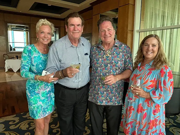Four adults standing indoors, smiling and holding drinks in a social setting.
