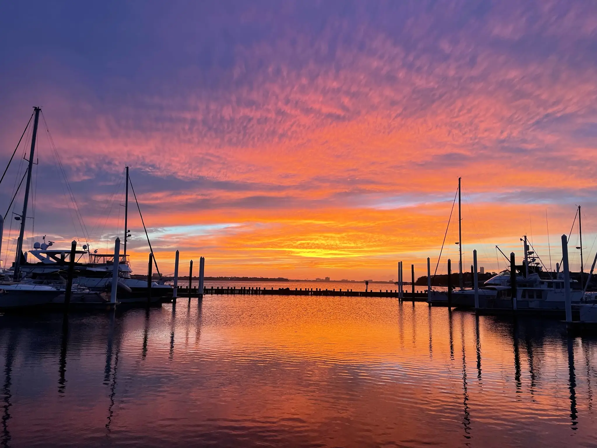 Harbor with sailboats and yachts at sunset reflecting vibrant orange and purple colors off calm water.