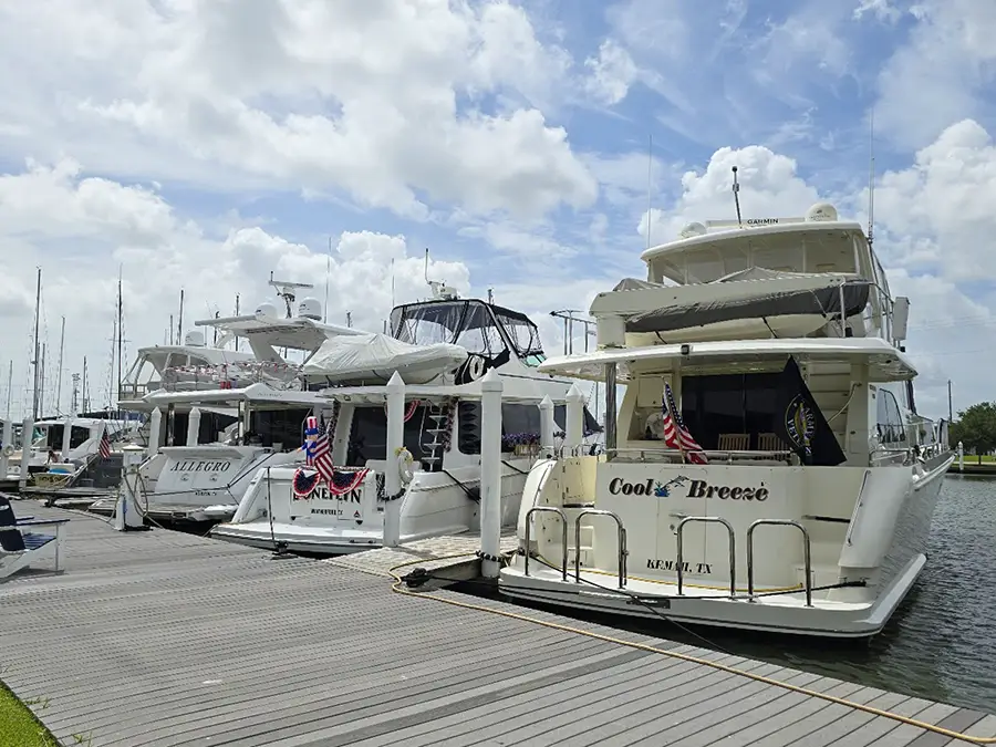 White yachts docked at a marina under a partly cloudy sky, with flags displayed on some boats.