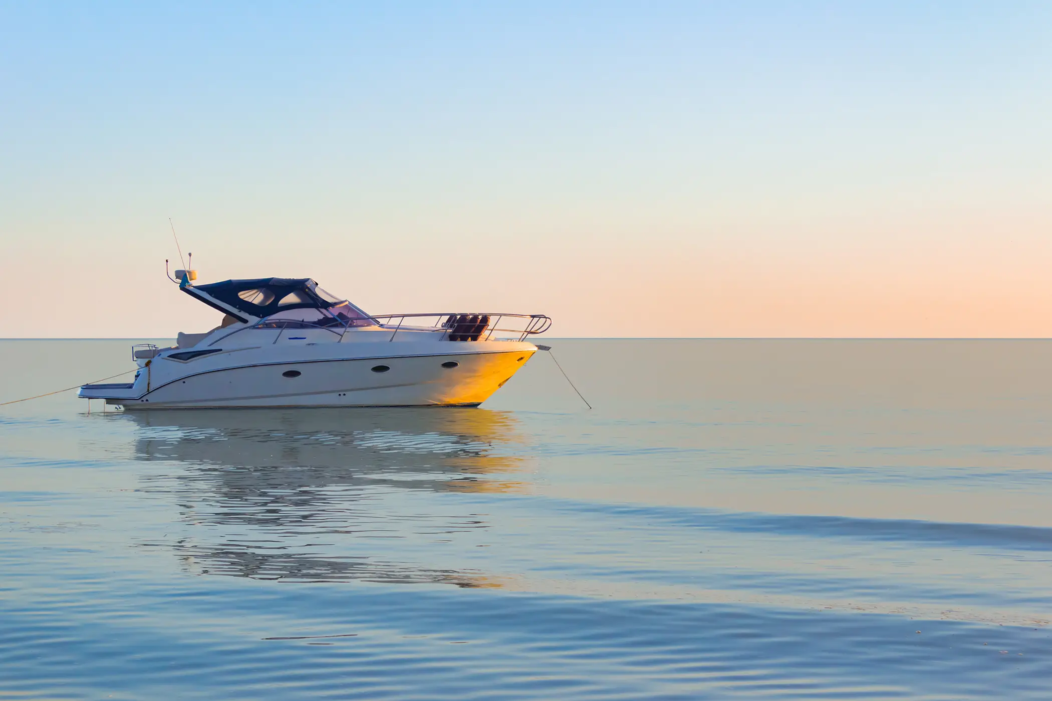 White motorboat anchored on calm water at sunset with soft pastel sky.