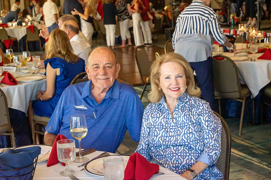 Smiling elderly man and woman seated at a restaurant table with wine and water glasses.