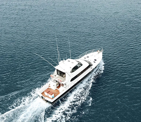 White yacht cruising on deep blue water with wake behind it.