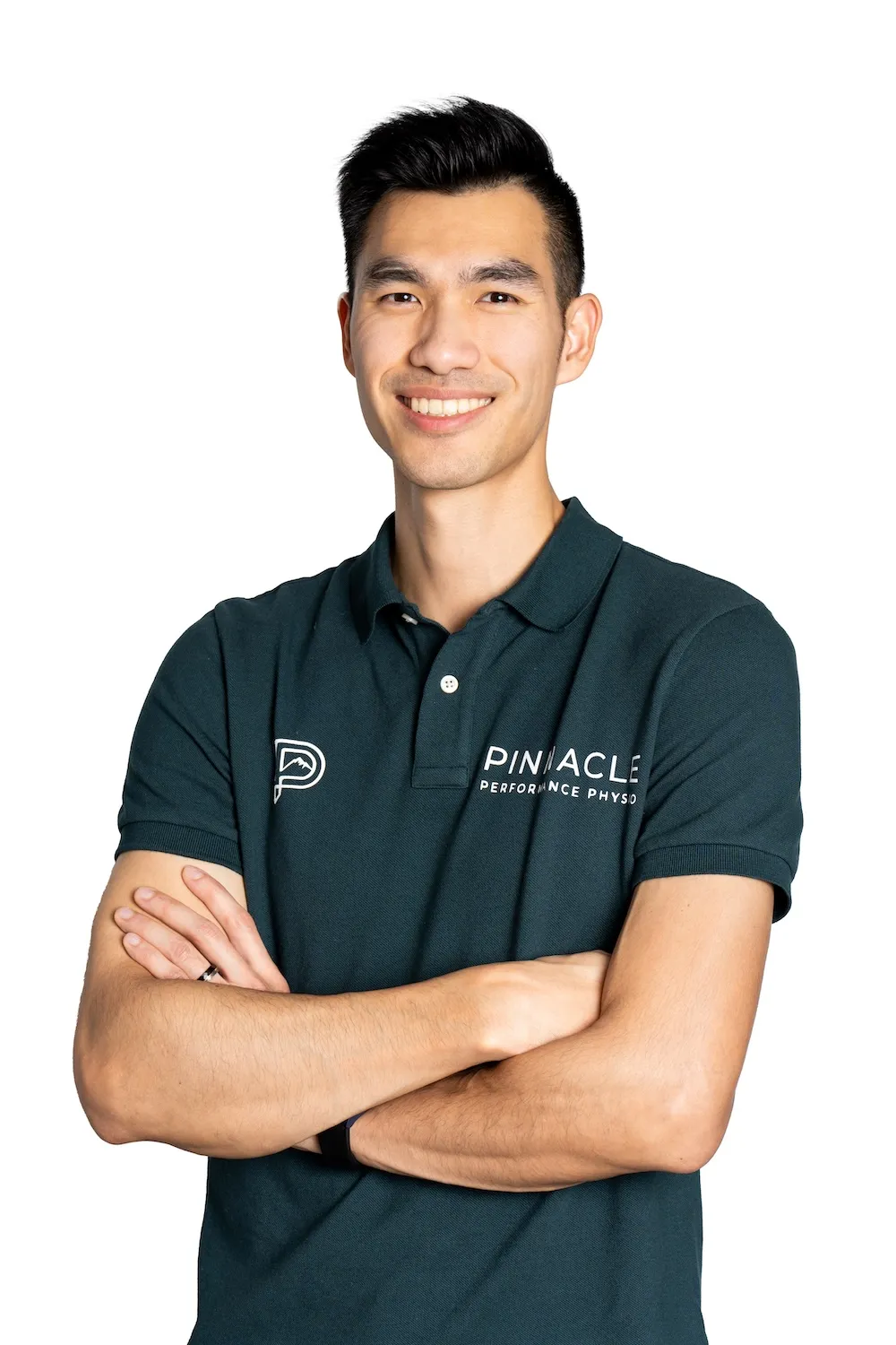 Smiling man with crossed arms wearing a dark green Pinnacle Performance Physio polo shirt.