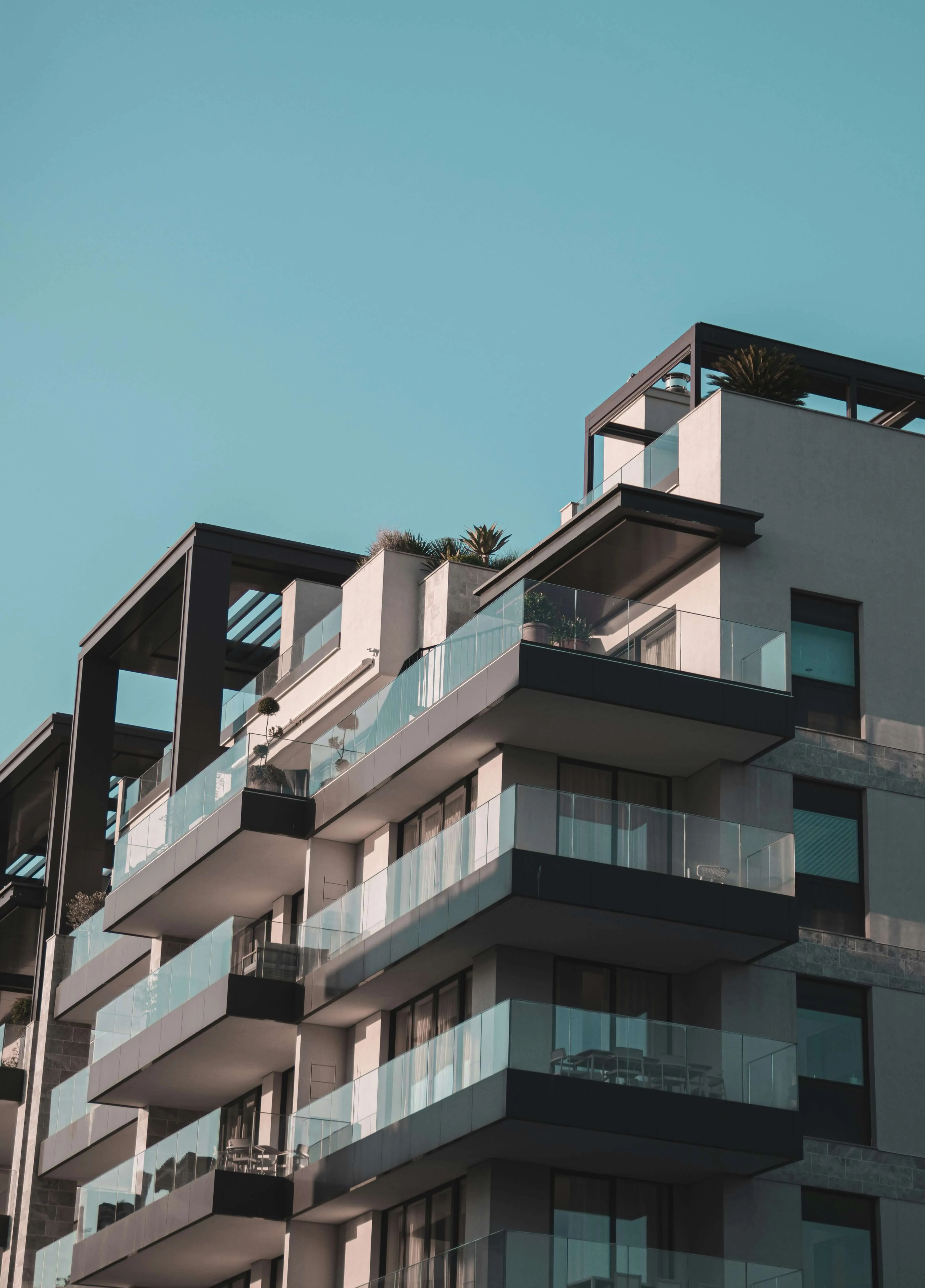 Modern apartment building with glass balconies under a clear blue sky.