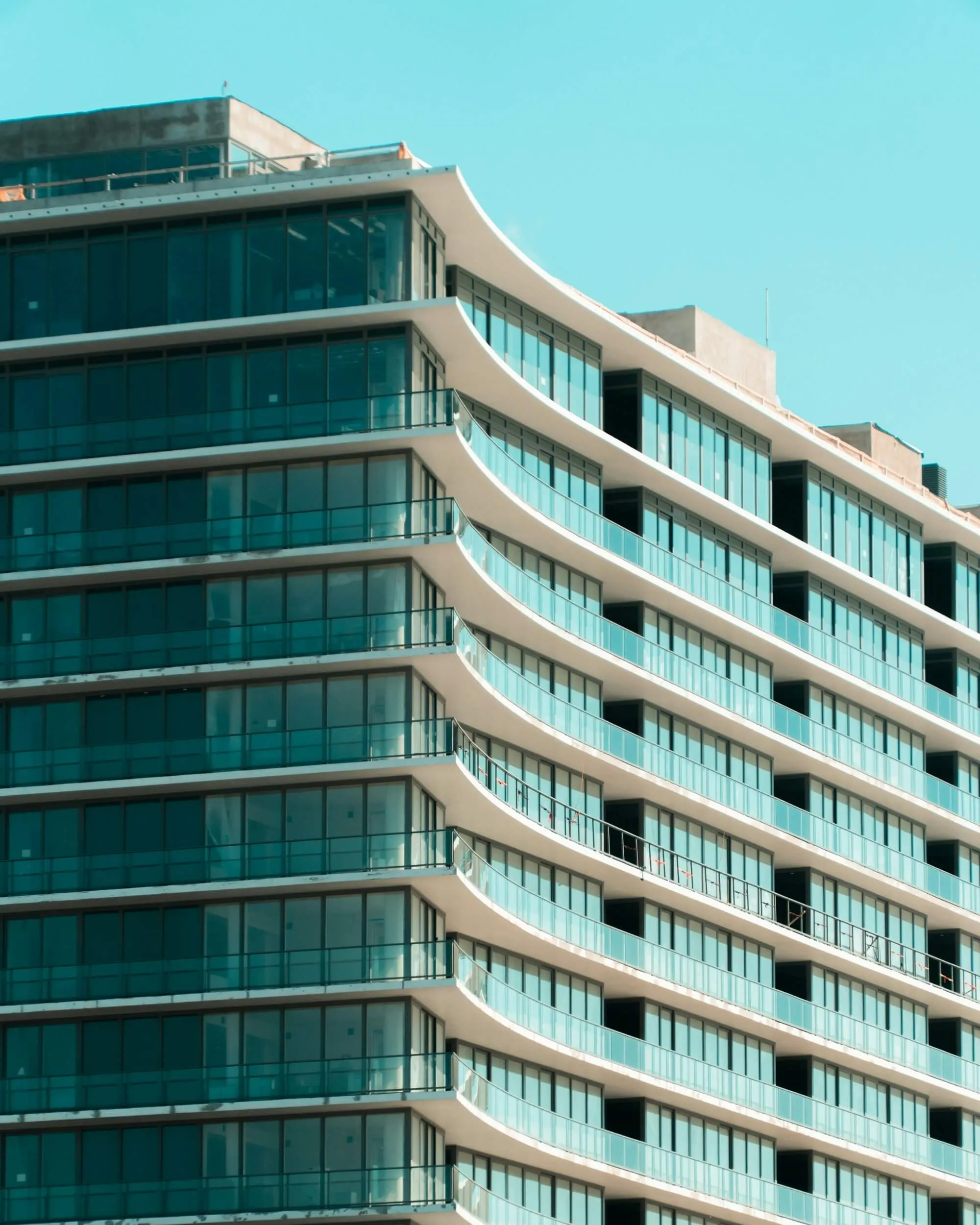 Modern building with curved balconies and large blue-tinted glass windows under clear blue sky.