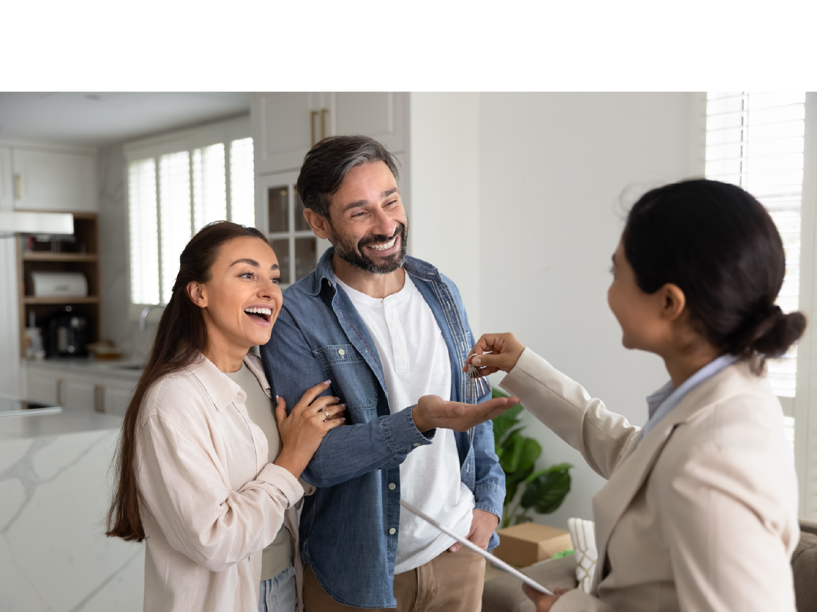 Un agente inmobiliario entrega las llaves de una casa a una pareja sonriente en una cocina moderna.