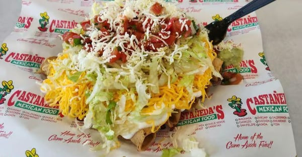 Mexican food plate with shredded cheese, lettuce, salsa, and meat on a branded Castaneda's Mexican Food paper.