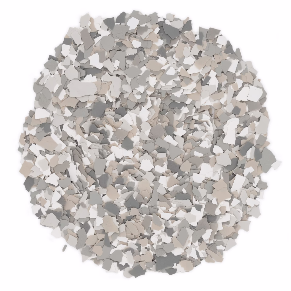 Pile of paint flakes in shades of gray, beige, and white arranged in a circular shape on a white background.