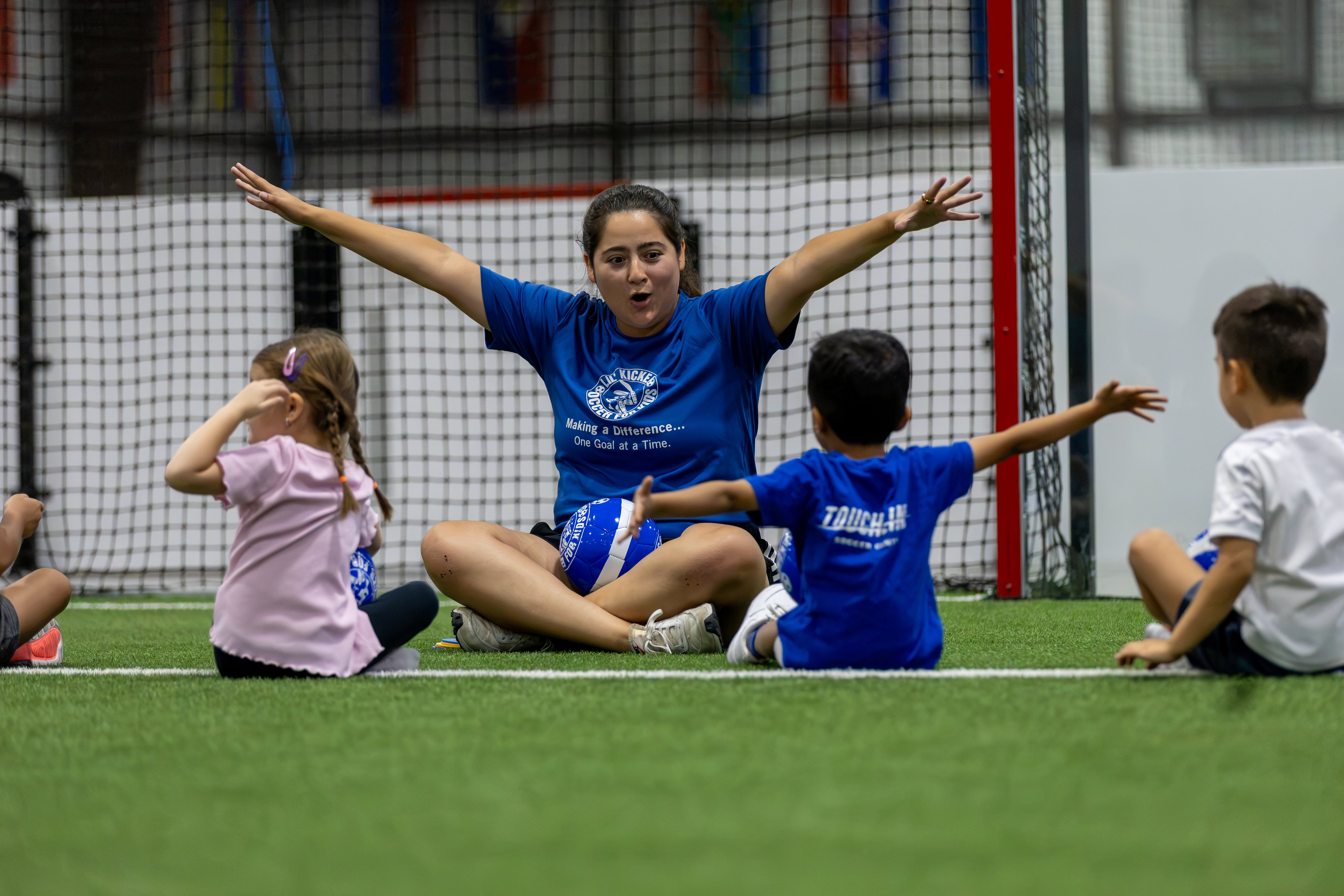 A Touchline coach leading young players through a class on indoor turf