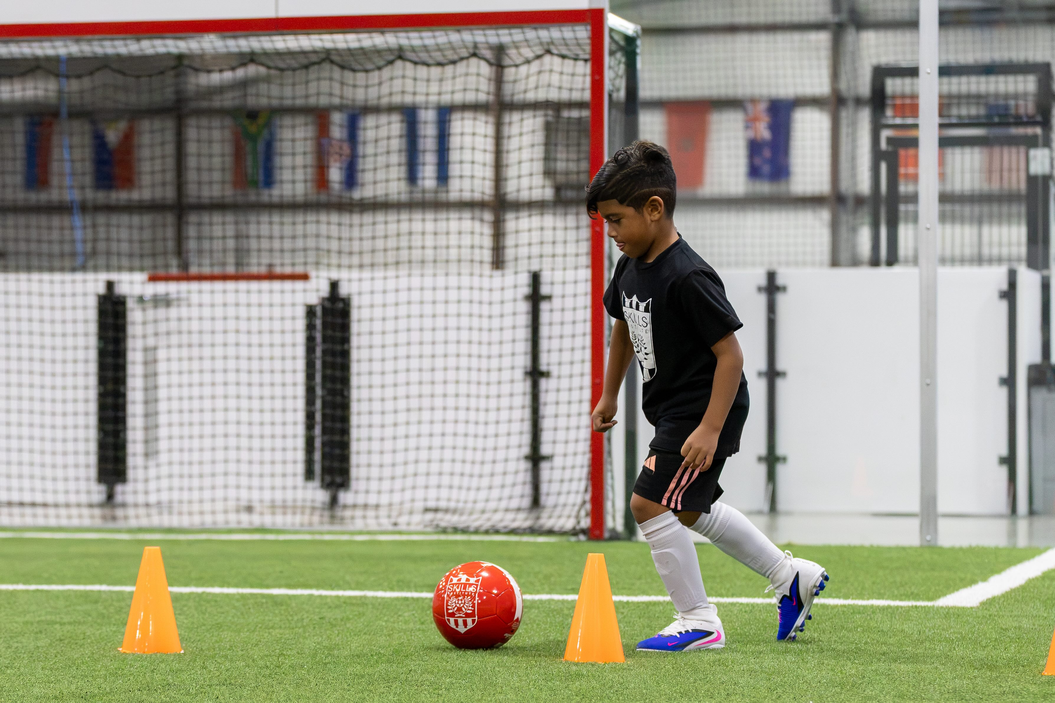 A young player dribbling through cones on indoor turf
