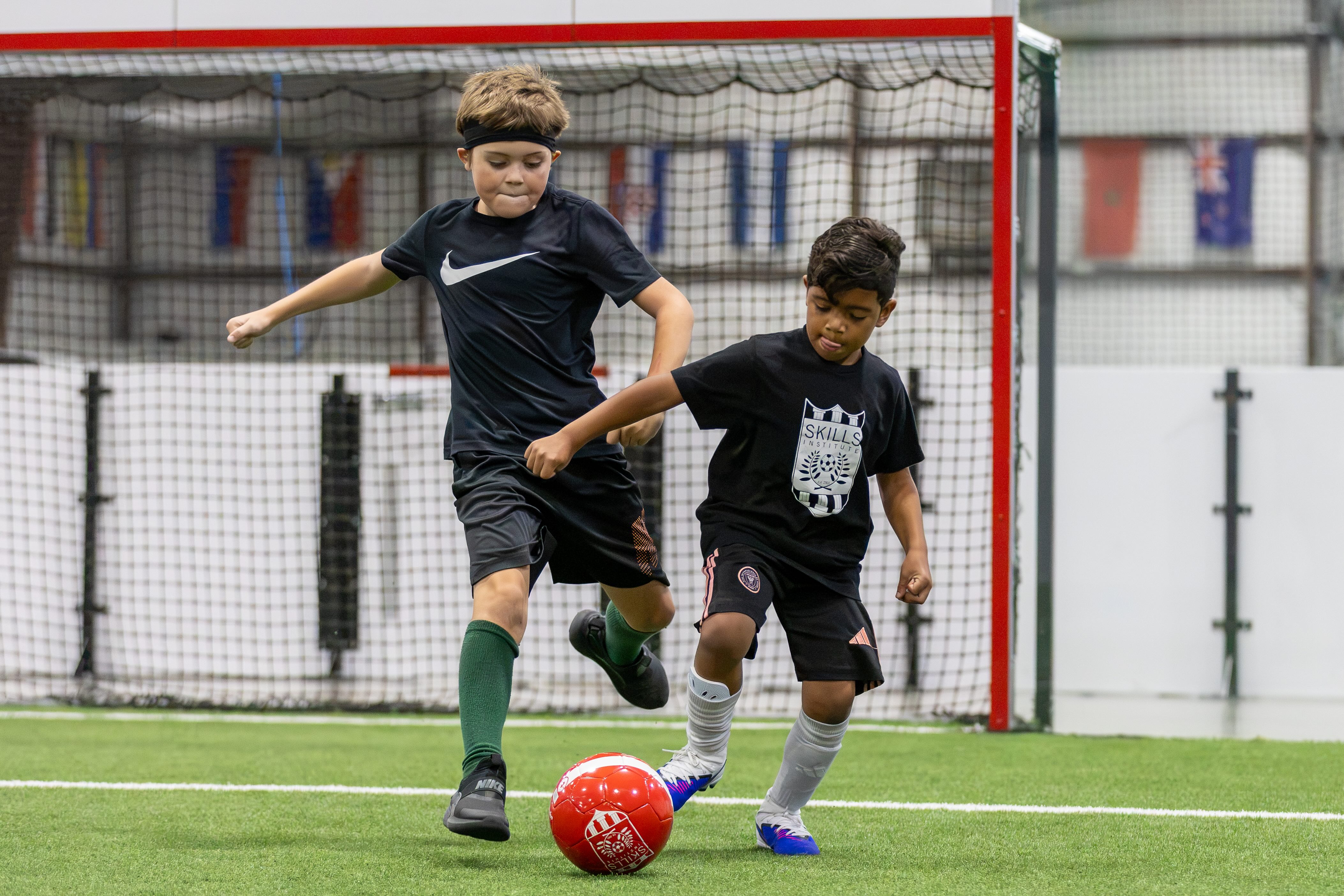 Two young players battling for the ball in front of a goal